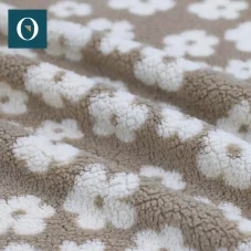 Teddy beránek ve světlé béžové barvě s jemným květinovým vzorem.