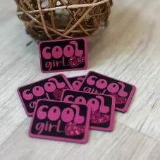 Černý koženkový štítek s růžovým nápisem Cool Girl a třpytivým srdíčkem – detail produktu.