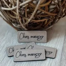 Koženkový štítek Chaos manager v béžové barvě s černým nápisem – detail produktu.