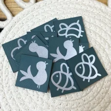 Koženkové štítky s reflexním ptáčkem a včelkou na petrolejovém podkladu.