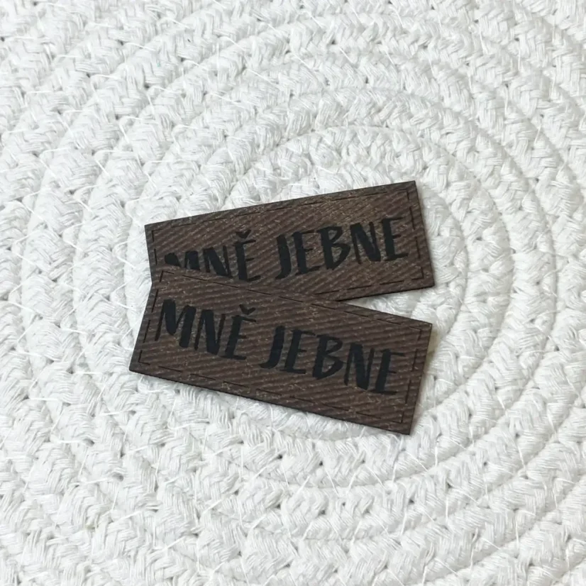 Koženkové štítky s nápisem „Mně jebne“ v červené, modré a hnědé barvě