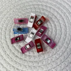 Deset barevných plastových kolíčků na látku s kovovou pružinou, položených na bílé podložce.