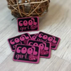 Černý koženkový štítek s růžovým nápisem Cool Girl a třpytivým srdíčkem – detail produktu.