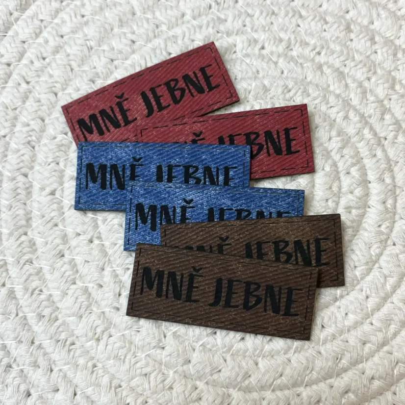 Koženkové štítky s nápisem „Mně jebne“ v červené, modré a hnědé barvě