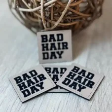 Koženkový štítek BAD HAIR DAY v béžové barvě s černým nápisem – detail produktu.