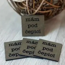 Koženkový štítek Mám pod čepicí v antik hnědé barvě s černým nápisem – detail produktu.