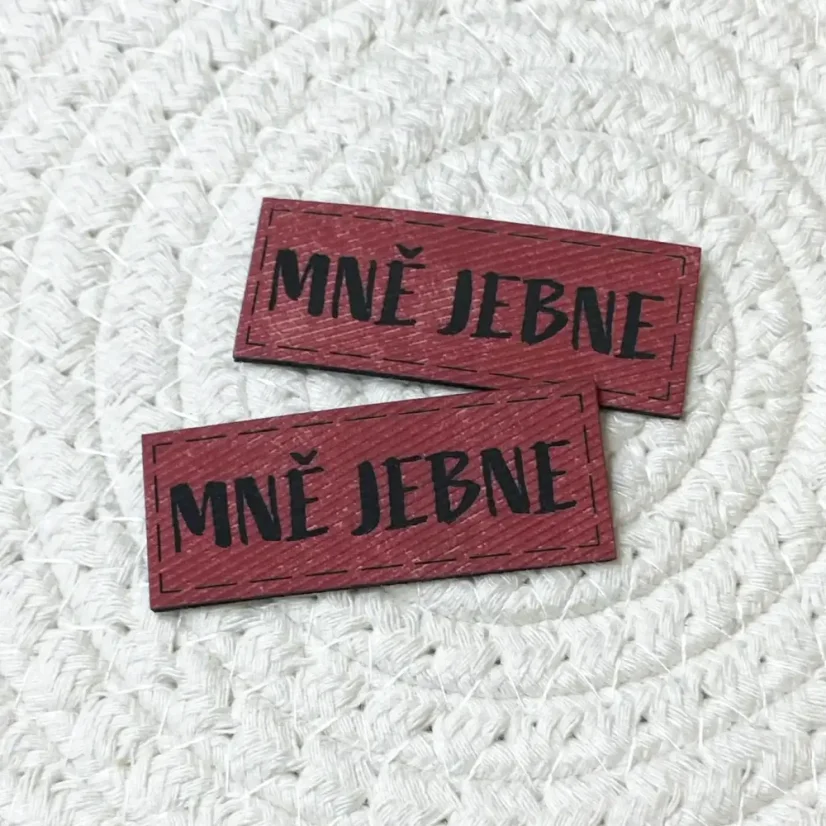 Koženkové štítky s nápisem „Mně jebne“ v červené, modré a hnědé barvě