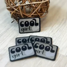 Reflexní koženkový štítek s nápisem Cool Girl a světle stříbrným srdíčkem – detail produktu.
